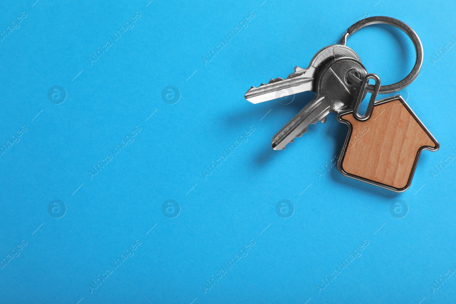 Photo of Keys with trinket in shape of house on blue background, top view and space for text. Real estate agent services