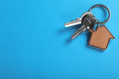 Keys with trinket in shape of house on blue background, top view and space for text. Real estate agent services