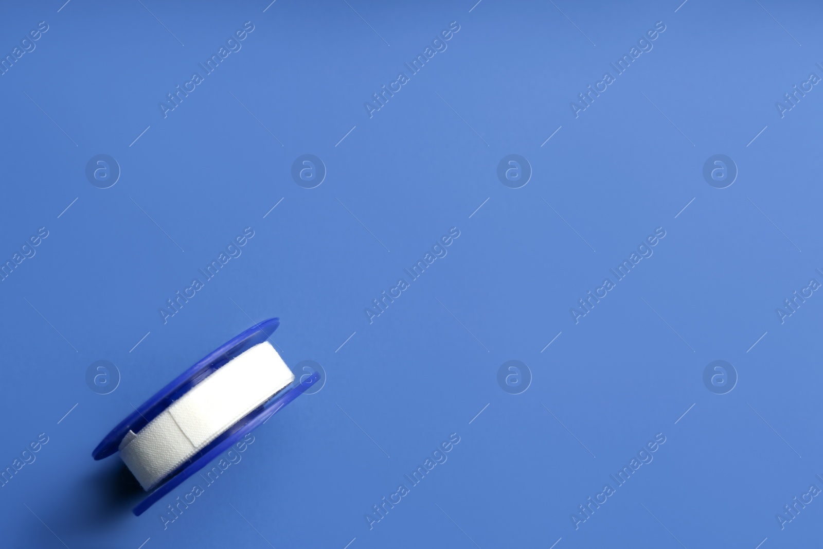 Photo of Sticking plaster roll on blue background, top view. Space for text