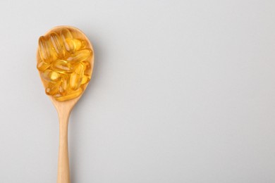 Vitamin capsules in wooden spoon on light background, top view. Space for text