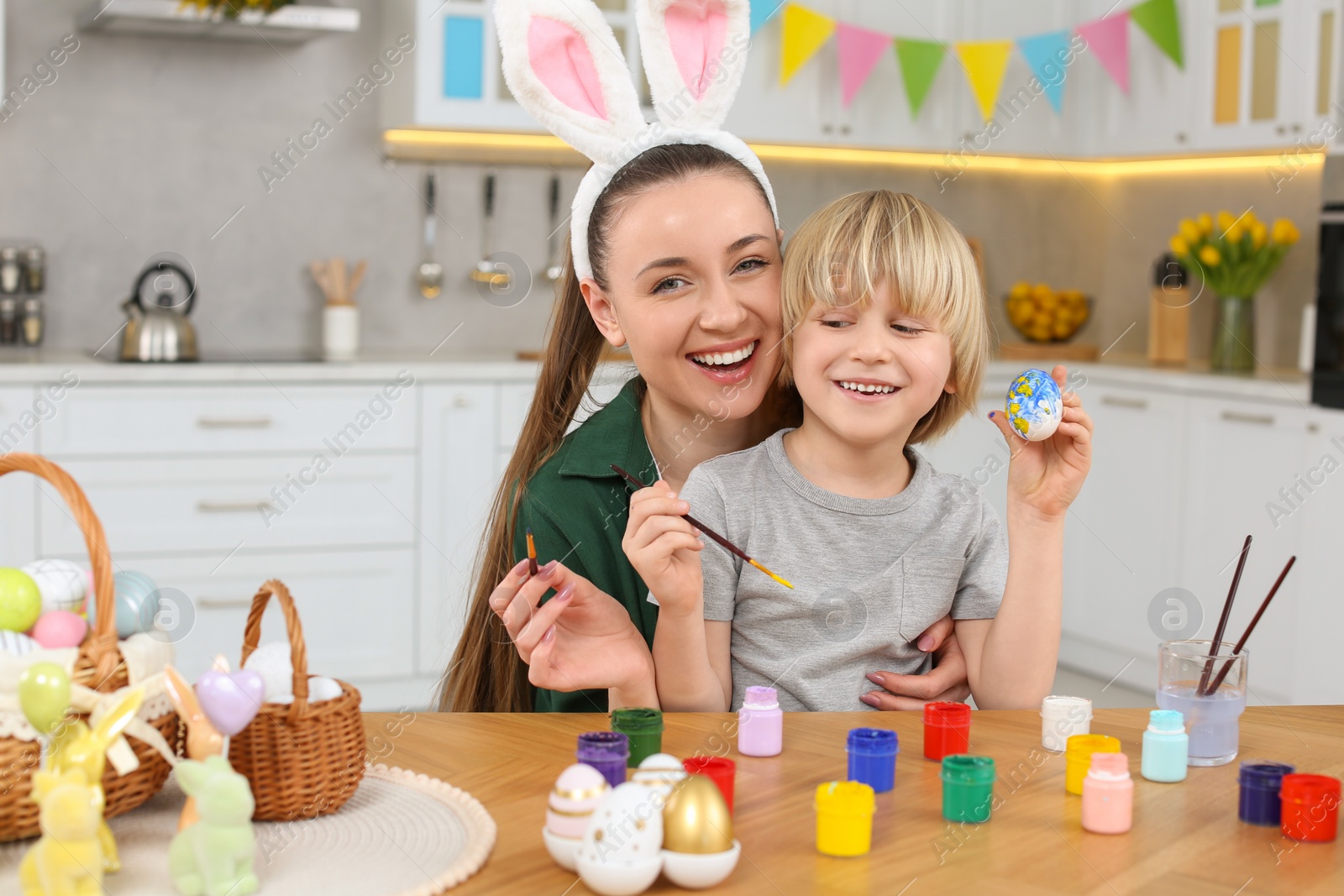 Photo of Mother and her son painting Easter eggs at table in kitchen