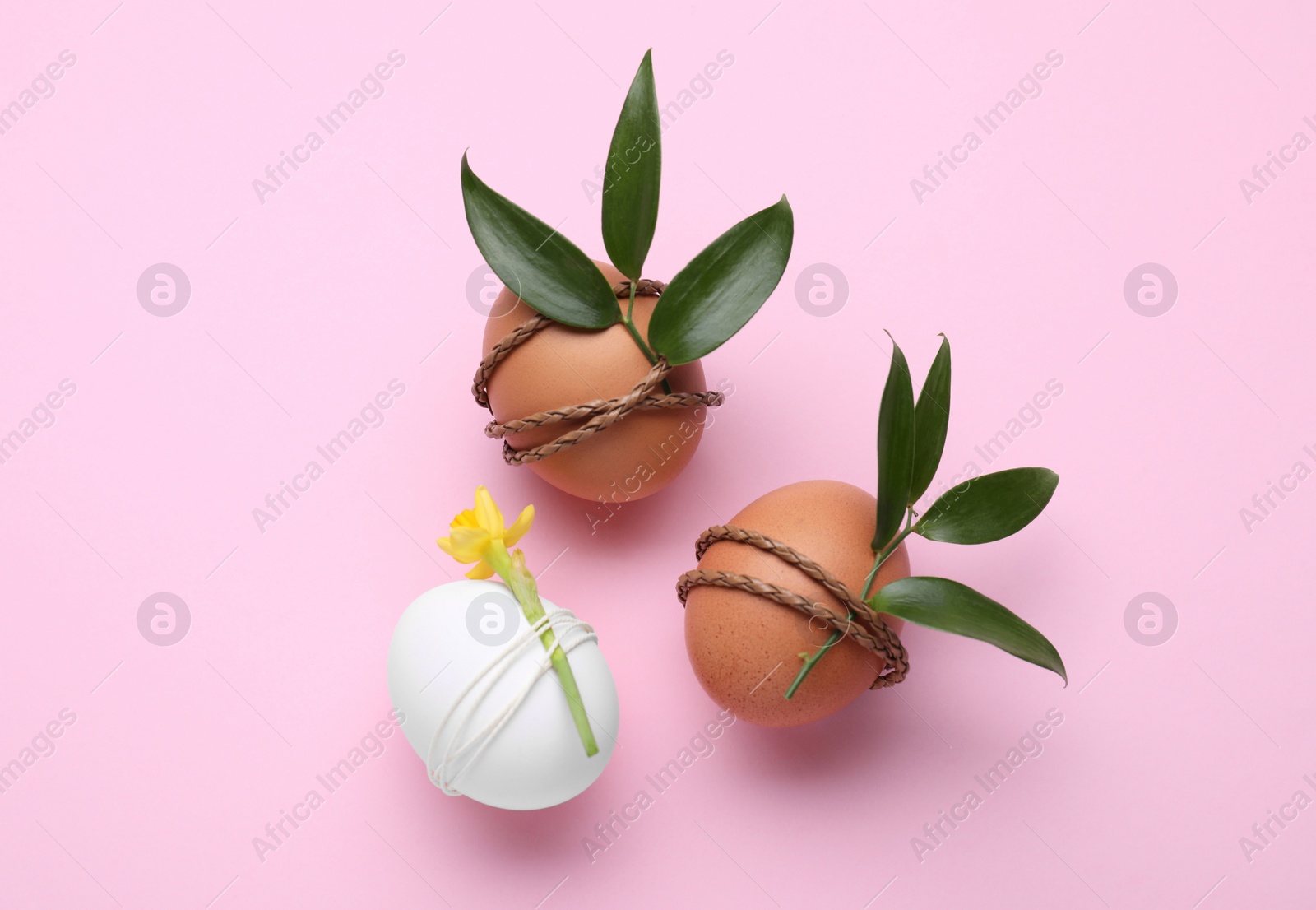 Photo of Easter eggs decorated with green leaves and flower on pink background, flat lay