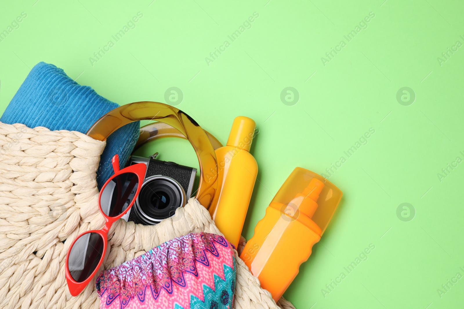 Photo of Knitted bag with beach objects on green background, flat lay. Space for text