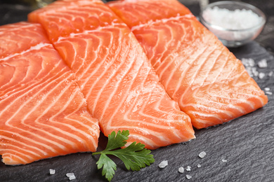 Photo of Fresh raw salmon with parsley and salt on slate plate, closeup. Fish delicacy