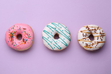 Different tasty glazed donuts on purple background, flat lay