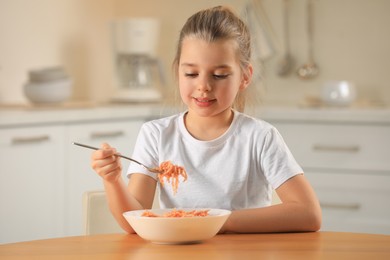 Cute little girl eating tasty pasta at table in kitchen