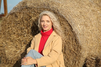 Photo of Beautiful woman sitting near hay bale outdoors. Autumn season