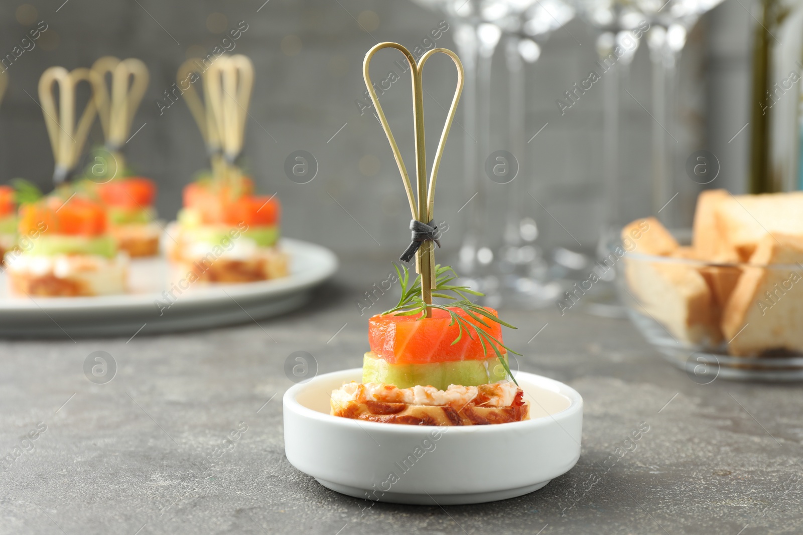 Photo of Tasty canape with salmon, cucumber, bread and cream cheese on grey table, closeup