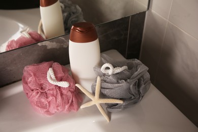 Photo of Colorful sponges between shower gel bottle and starfish on sink in bathroom