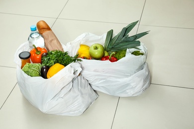 Photo of White plastic bags with vegetables and other products on floor