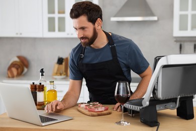 Man making dinner while watching online cooking course via laptop in kitchen