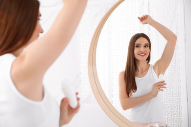 Photo of Beautiful young woman applying deodorant in bathroom