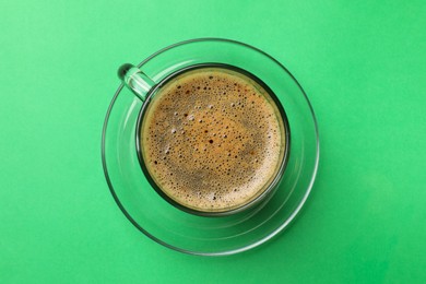 Photo of Aromatic coffee in glass cup on green background, top view