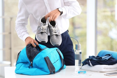 Photo of Young businessman packing sports stuff for training into bag in office