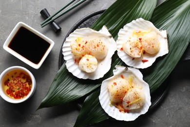 Photo of Raw scallops with spices, lemon zest, shells and sauces on grey textured table, flat lay
