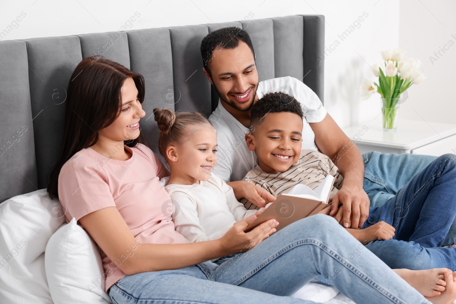 Photo of Happy international family reading book on bed