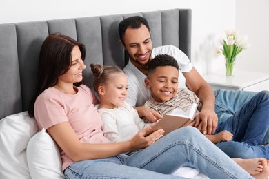 Photo of Happy international family reading book on bed