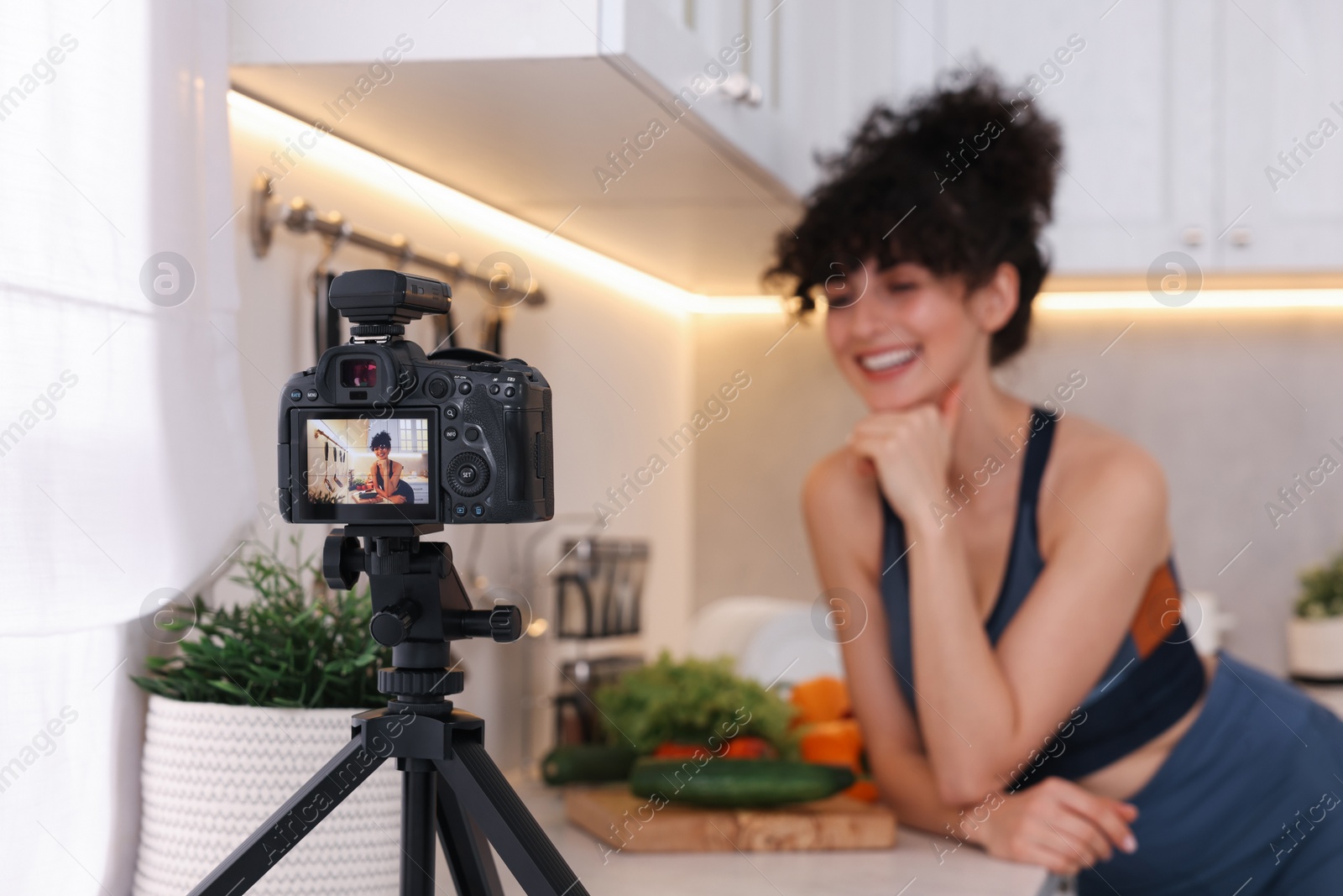 Photo of Food blogger explaining something while recording video in kitchen, focus on camera