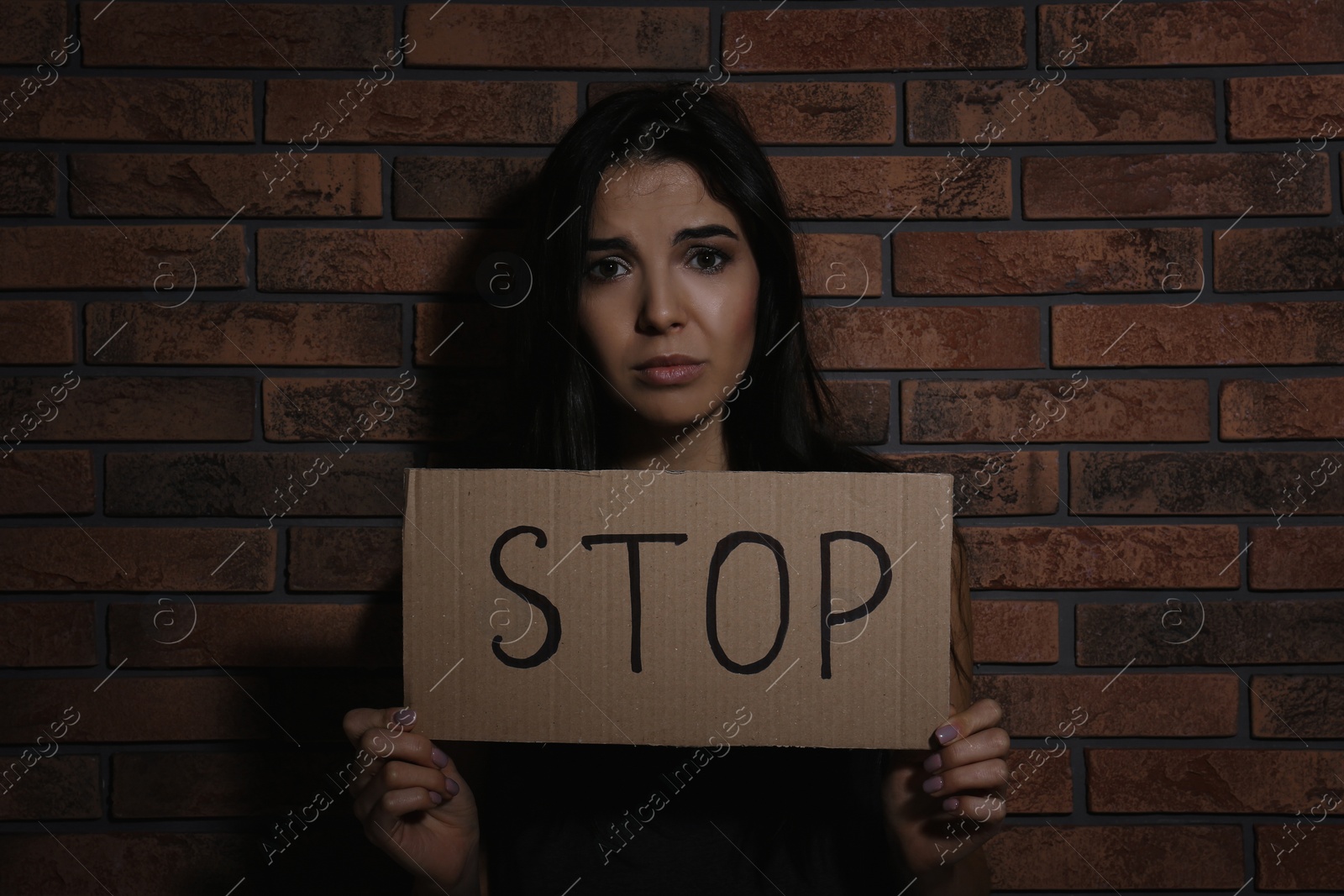 Photo of Abused young woman with sign STOP near brick wall. Domestic violence concept