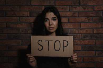 Abused young woman with sign STOP near brick wall. Domestic violence concept