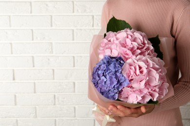 Photo of Woman with bouquet of beautiful hortensia flowers near white brick wall, closeup. Space for text