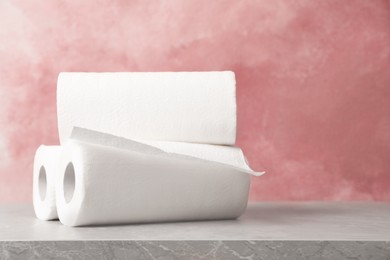 Photo of Rolls of white paper towels on grey table near pink wall. Space for text