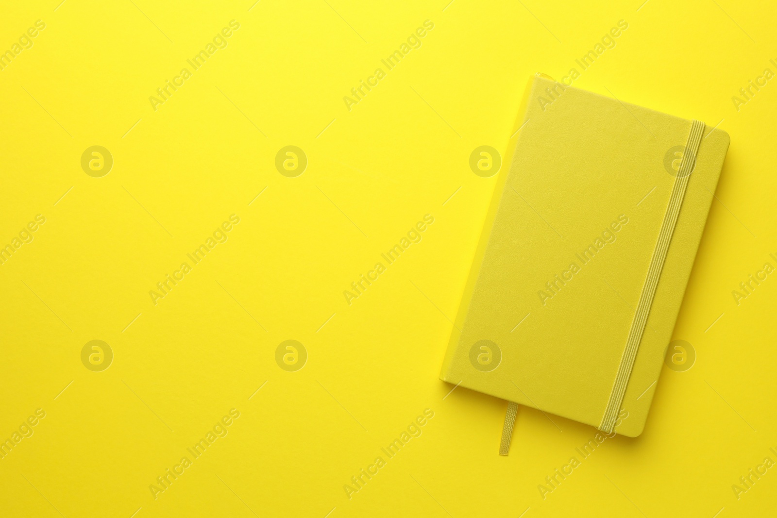 Photo of Closed notebook on yellow background, top view. Space for text