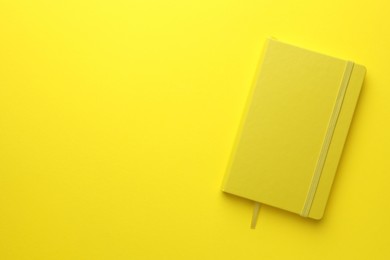 Photo of Closed notebook on yellow background, top view. Space for text