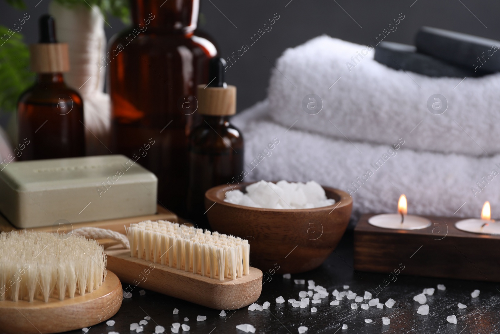 Photo of Spa composition. Brushes, soap bar, sea salt and burning candles on black table, closeup