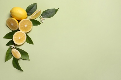 Many fresh ripe lemons with leaves and flowers on light green background, flat lay. Space for text