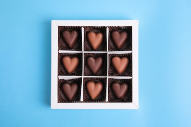 Tasty heart shaped chocolate candies on light blue background, top view. Happy Valentine's day