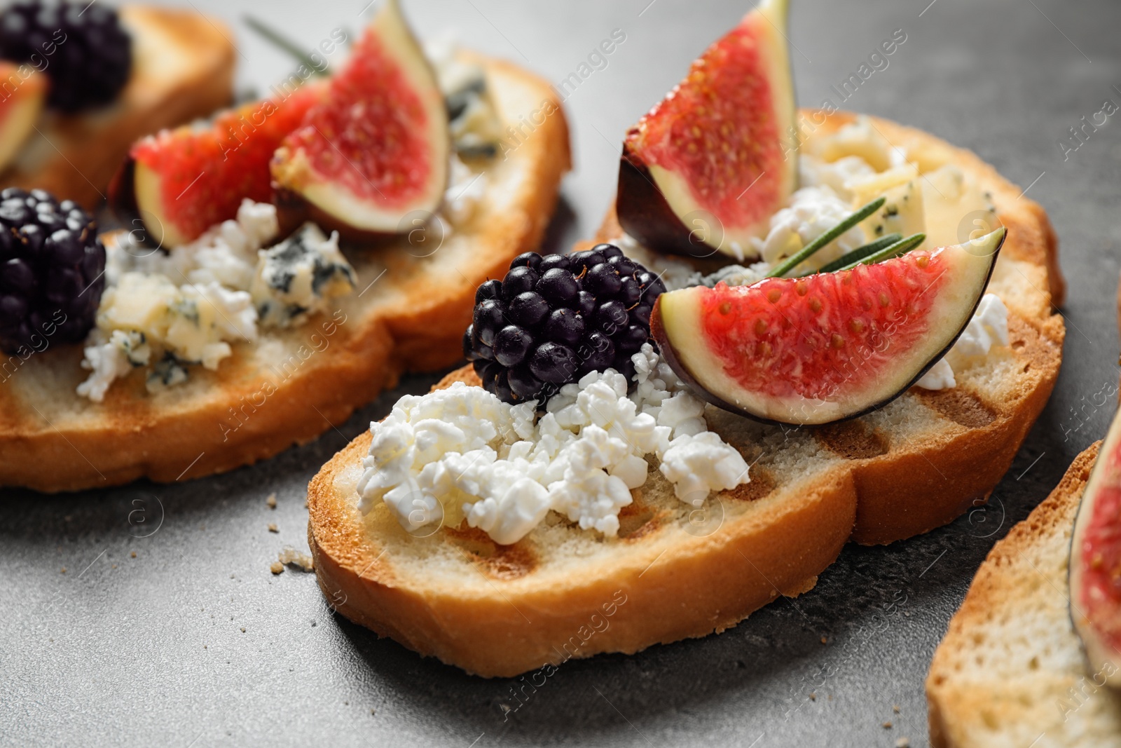 Photo of Bruschettas with cheese, figs and blackberries on grey table, closeup