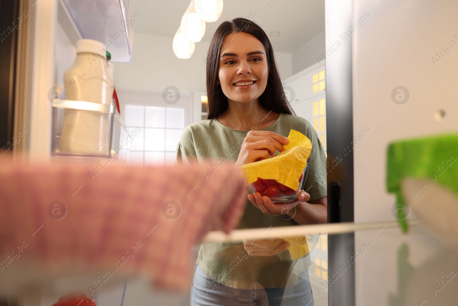 Photo of Happy woman taking away beeswax food wrap, view from refrigerator