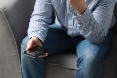 Photo of Man holding damaged smartphone while sitting on armchair, closeup. Device repairing