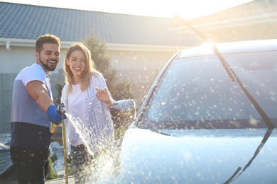 Photo of Happy young couple washing car at backyard on sunny day
