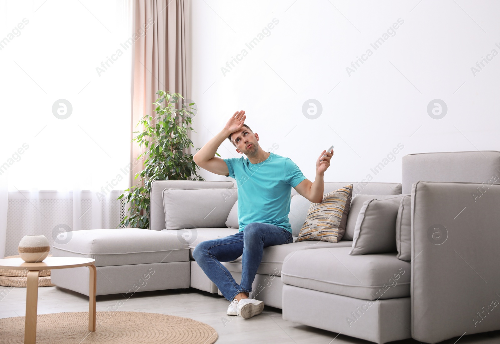 Photo of Young man with remote control suffering from heat under broken air conditioner at home