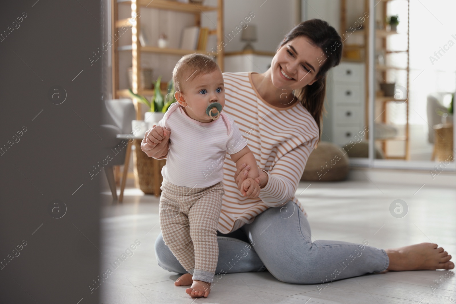 Photo of Mother supporting her baby daughter while she learning to walk at home