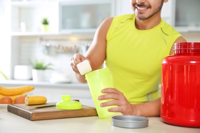 Photo of Young man preparing protein shake at table in kitchen, closeup. Space for text