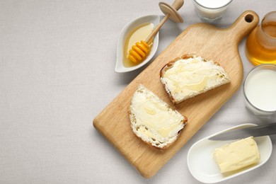 Slices of bread with butter, honey and milk on white table, flat lay. Space for text