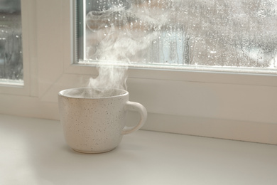 Photo of Cup of hot drink near window on rainy day.  Space for text