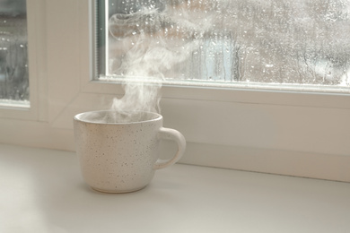 Cup of hot drink near window on rainy day.  Space for text