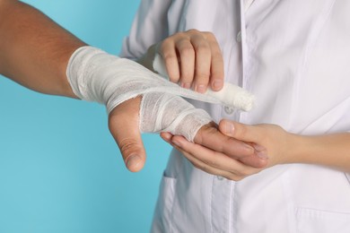 Photo of Doctor applying bandage onto patient's hand on light blue background, closeup