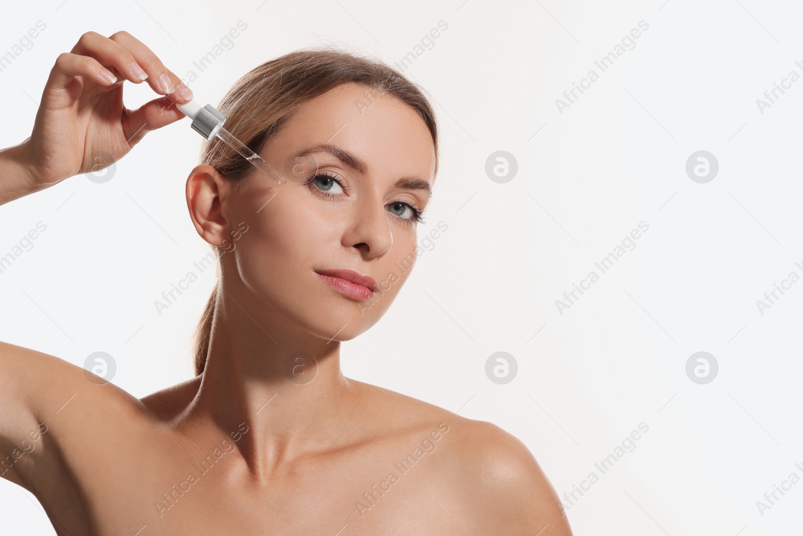 Photo of Beautiful woman applying cosmetic serum onto her face on white background, space for text