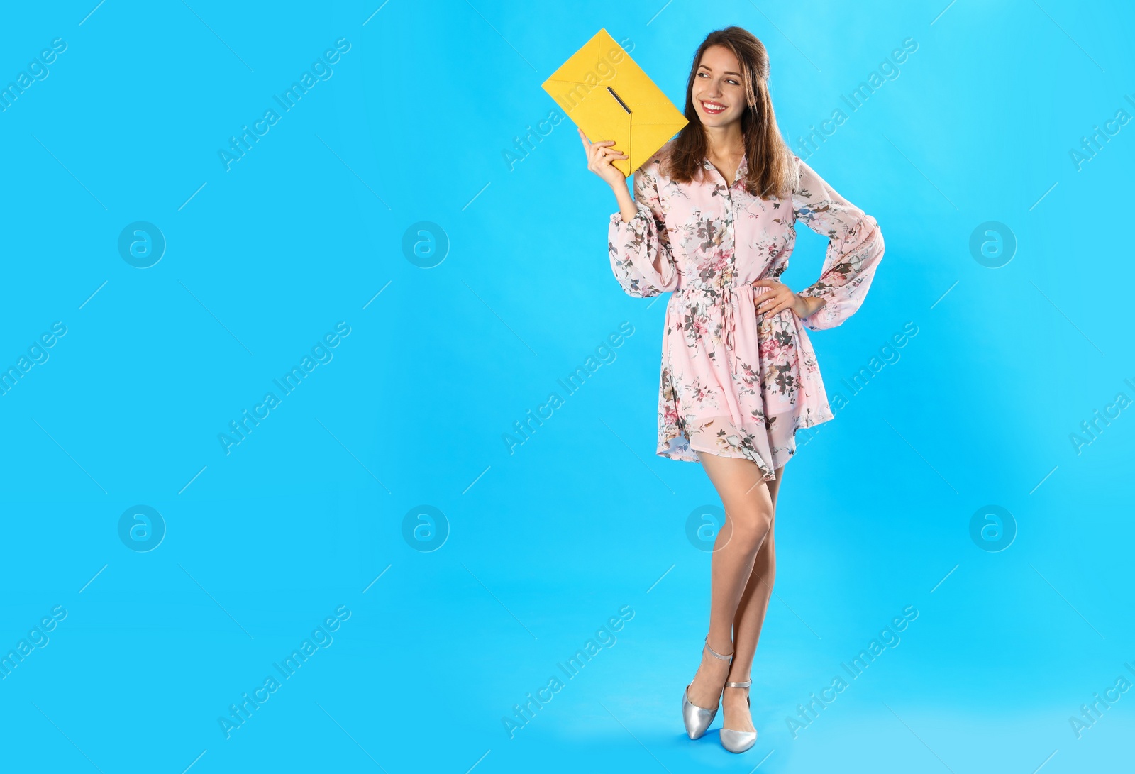 Photo of Young woman wearing floral print dress with elegant clutch on light blue background