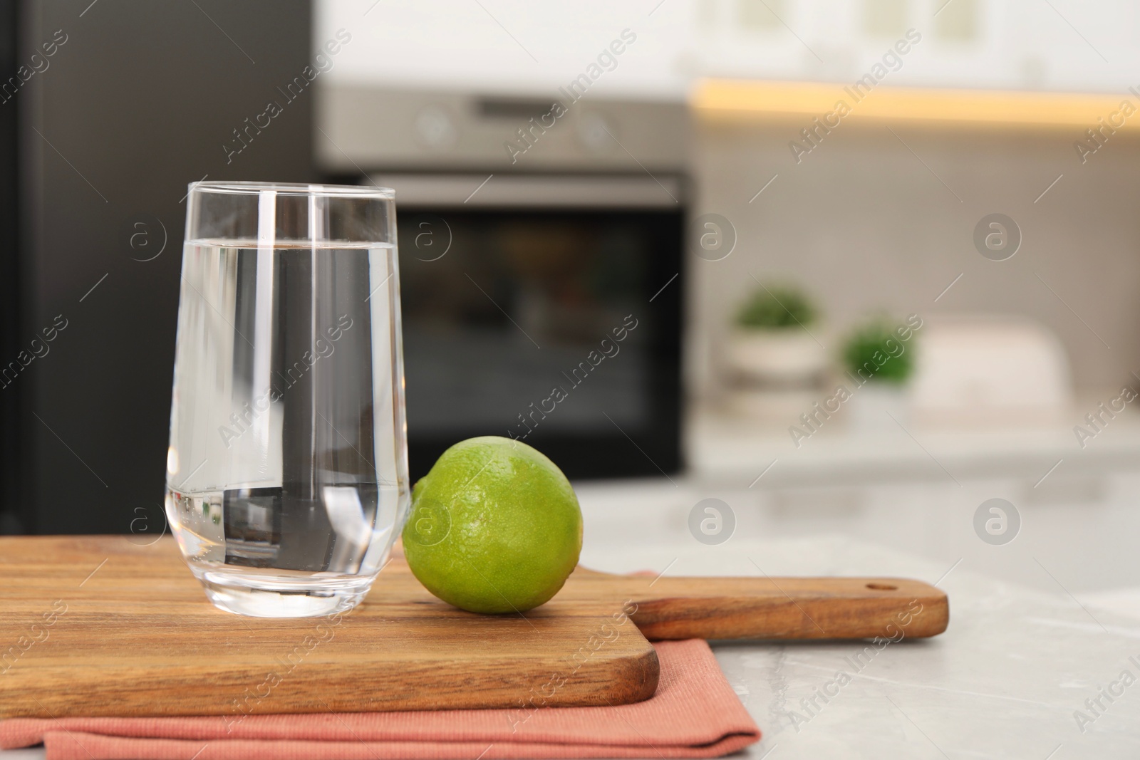 Photo of Filtered water in glass and lime on light marble table in kitchen, closeup. Space for text