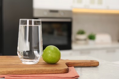 Photo of Filtered water in glass and lime on light marble table in kitchen, closeup. Space for text