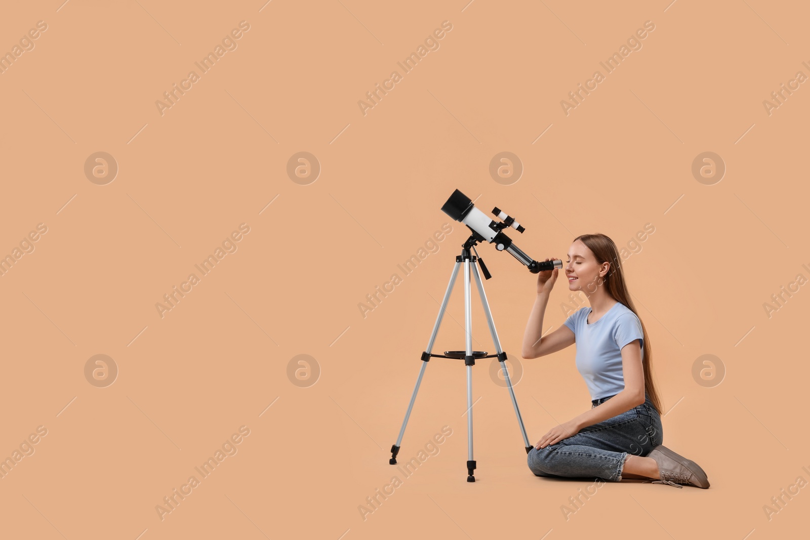 Photo of Young astronomer looking at stars through telescope on beige background, space for text