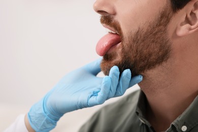 Doctor examining man`s oral cavity on light grey background, closeup. Space for text