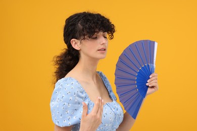 Photo of Woman with hand fan suffering from heat on orange background