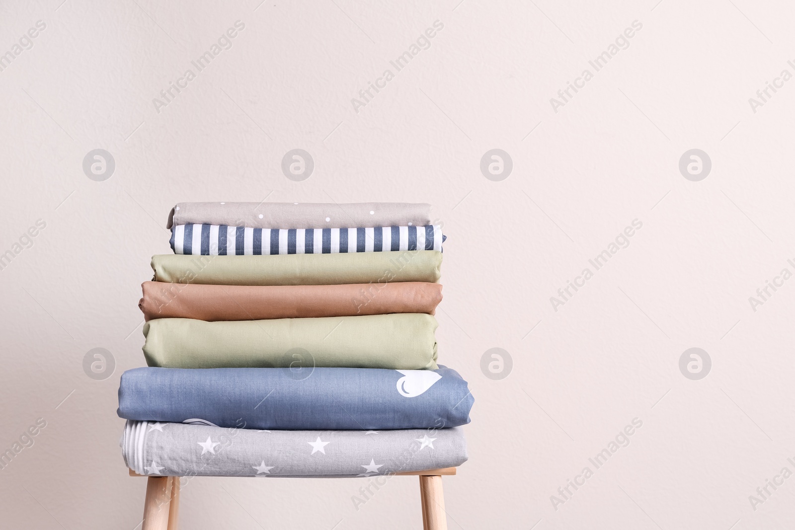 Photo of Stack of clean bed sheets on stool near beige wall. Space for text